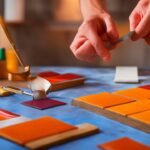 A focused close-up of a person’s hands carefully peeling adhesive backing off a stylish tile panel and applying it to a kitchen wall, surrounded by scattered tools like scissors and a level, illuminated with warm cinematic lighting and rich colors that highlight the texture of the backsplash and evoke a determined, creative DIY spirit in a realistic, editorial photographic style with shallow depth of field.