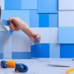 A determined homeowner’s hands carefully peeling and aligning modern geometric peel-and-stick backsplash tiles on a kitchen wall, surrounded by scissors, a tape measure, and a utility knife, captured in cinematic lighting with rich colors and shallow depth of field for an intense, editorial close-up moment of DIY transformation.