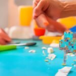 A close-up cinematic shot of hands carefully peeling and aligning a stylish peel-and-stick backsplash tile on a kitchen wall, with scattered tiles, a utility knife, measuring tape, and soft natural light highlighting the focused, determined expression of a homeowner mid-DIY makeover, captured with rich colors and shallow depth of field.