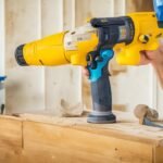 Cinematic editorial photo of a determined homeowner wearing work gloves and using a cordless drill to install floating shelves against a freshly painted wall in natural light, with scattered tools and peel-and-stick backsplash materials on a drop cloth nearby, intense focus and rich warm tones highlighting the hands-on DIY home upgrade process.