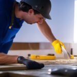 A determined homeowner wearing gloves intensely applying peel-and-stick backsplash tiles in a brightly lit kitchen, surrounded by modern DIY tools like a utility knife, level, and caulking gun, captured with cinematic lighting and a shallow depth of field that highlights focused hands and textured surfaces in rich, warm tones.